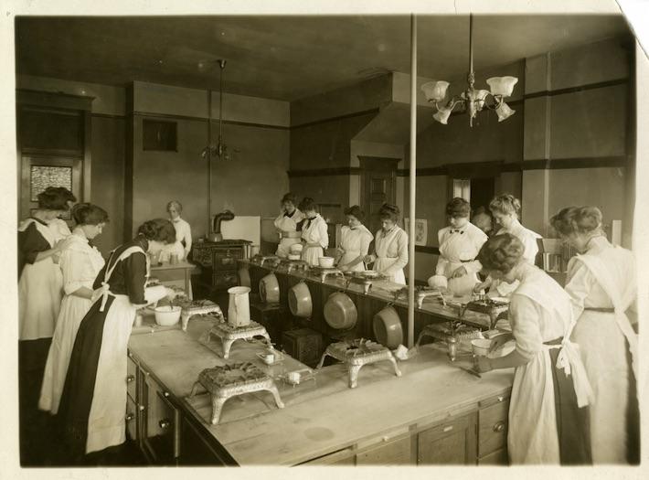  A black and white photo of students in a home ec class in the early 20th Century