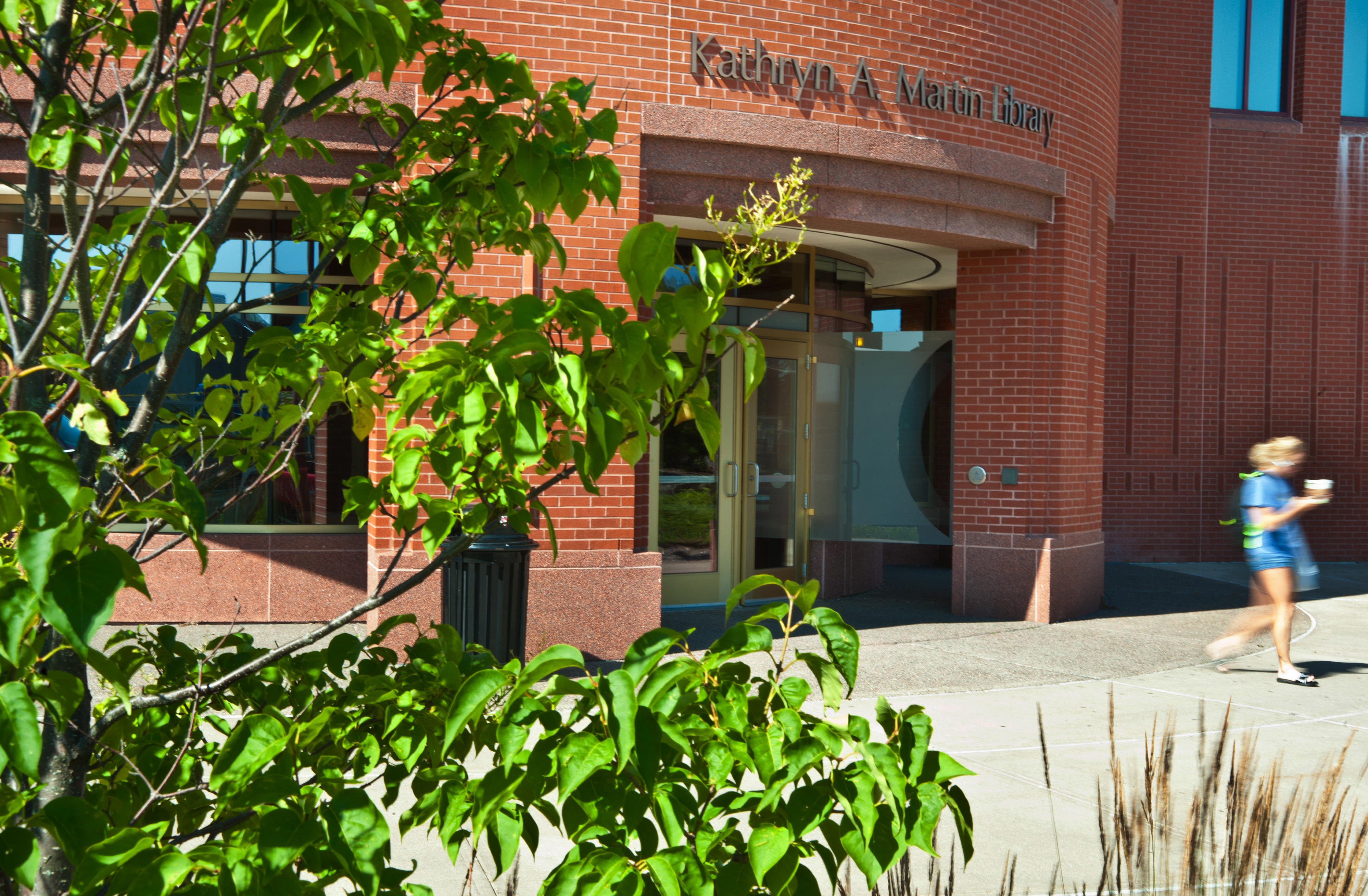 A building with a sign reading "Kathryn A. Martin Library." A student is walking past.