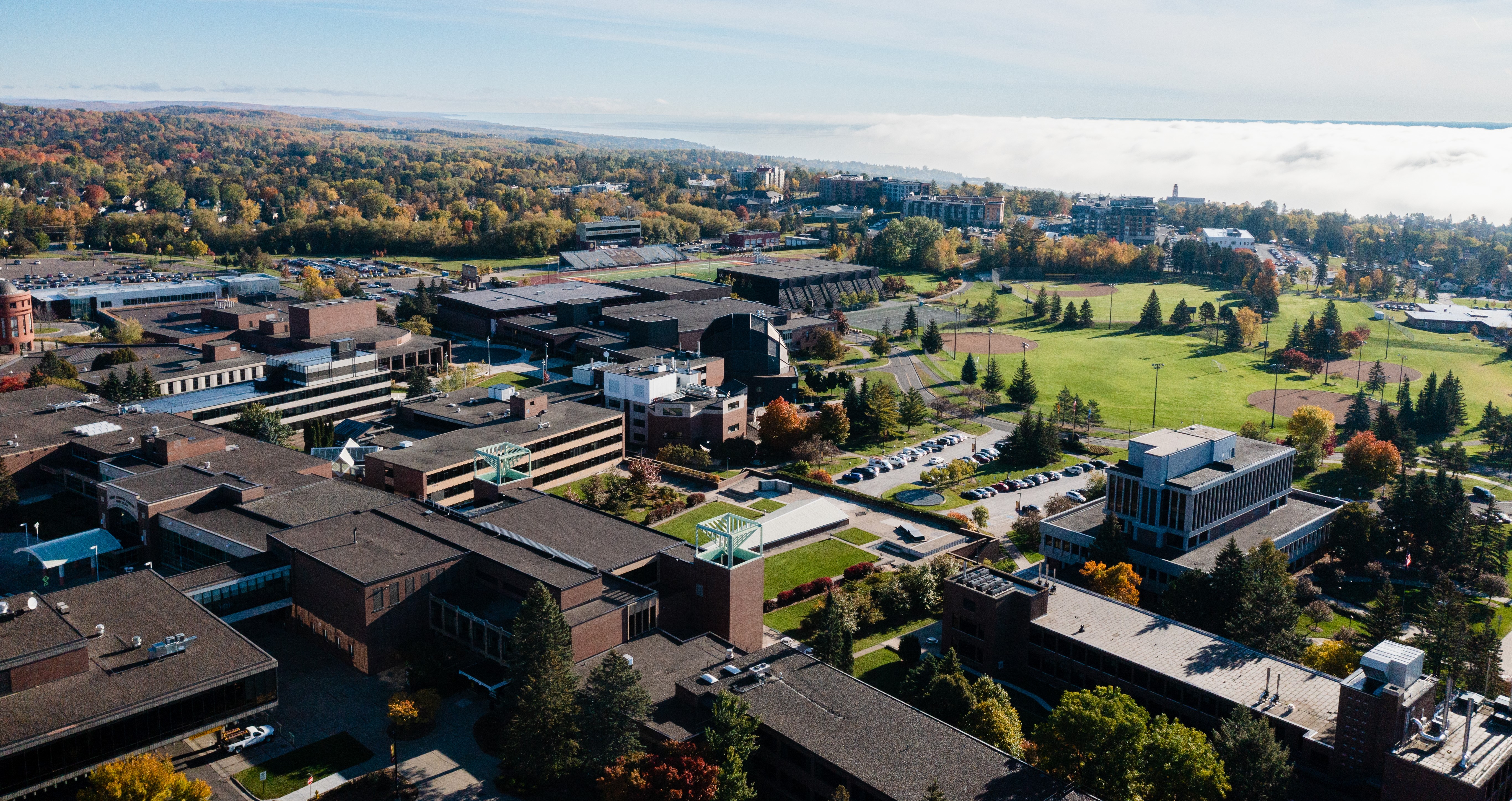 Aerial view of campus, showcasing various buildings, greenspace, and a spectacular cloud inversion over Lake Superior