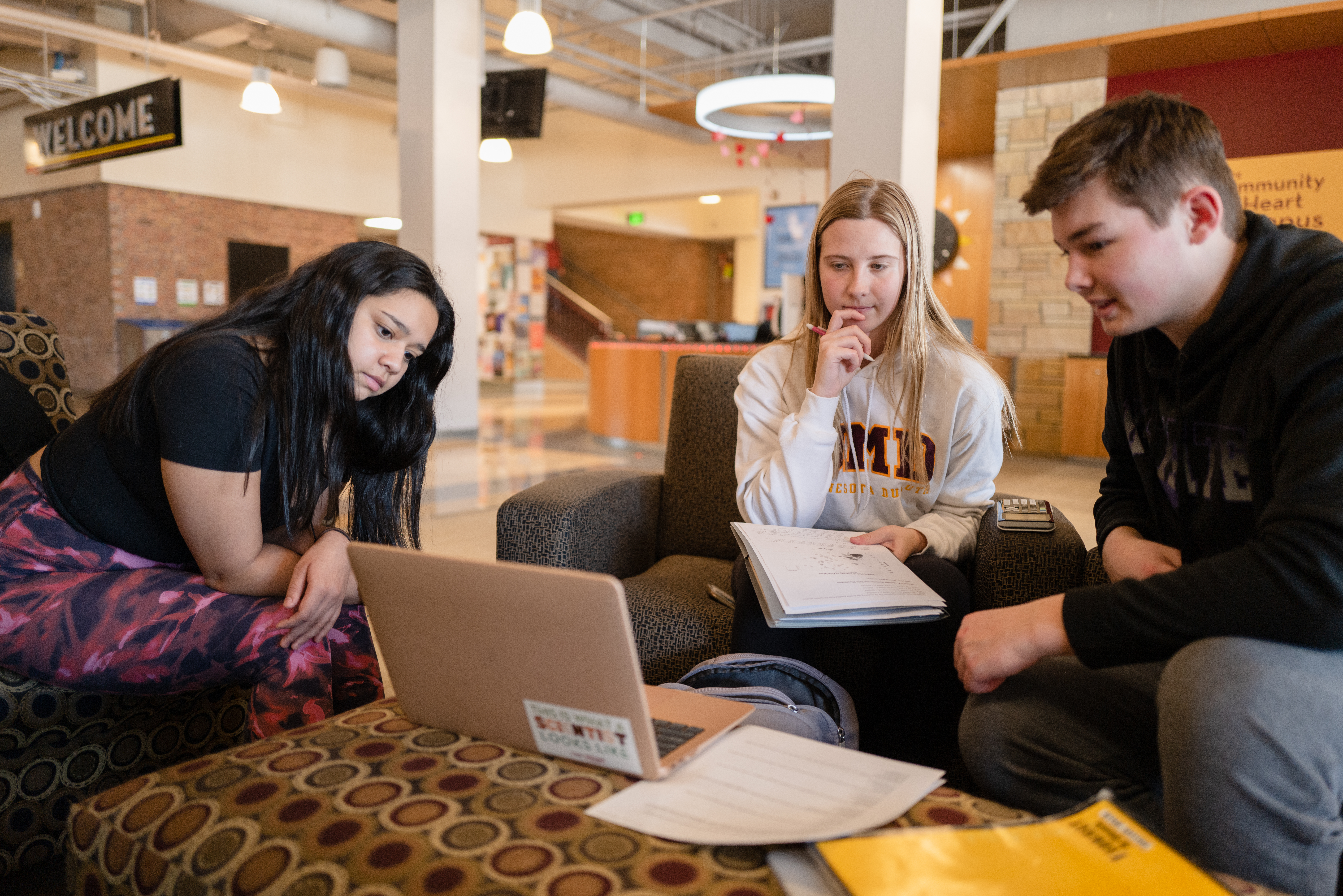 Three students study in the Kirby Student Center with notebooks, calculators, and a laptop