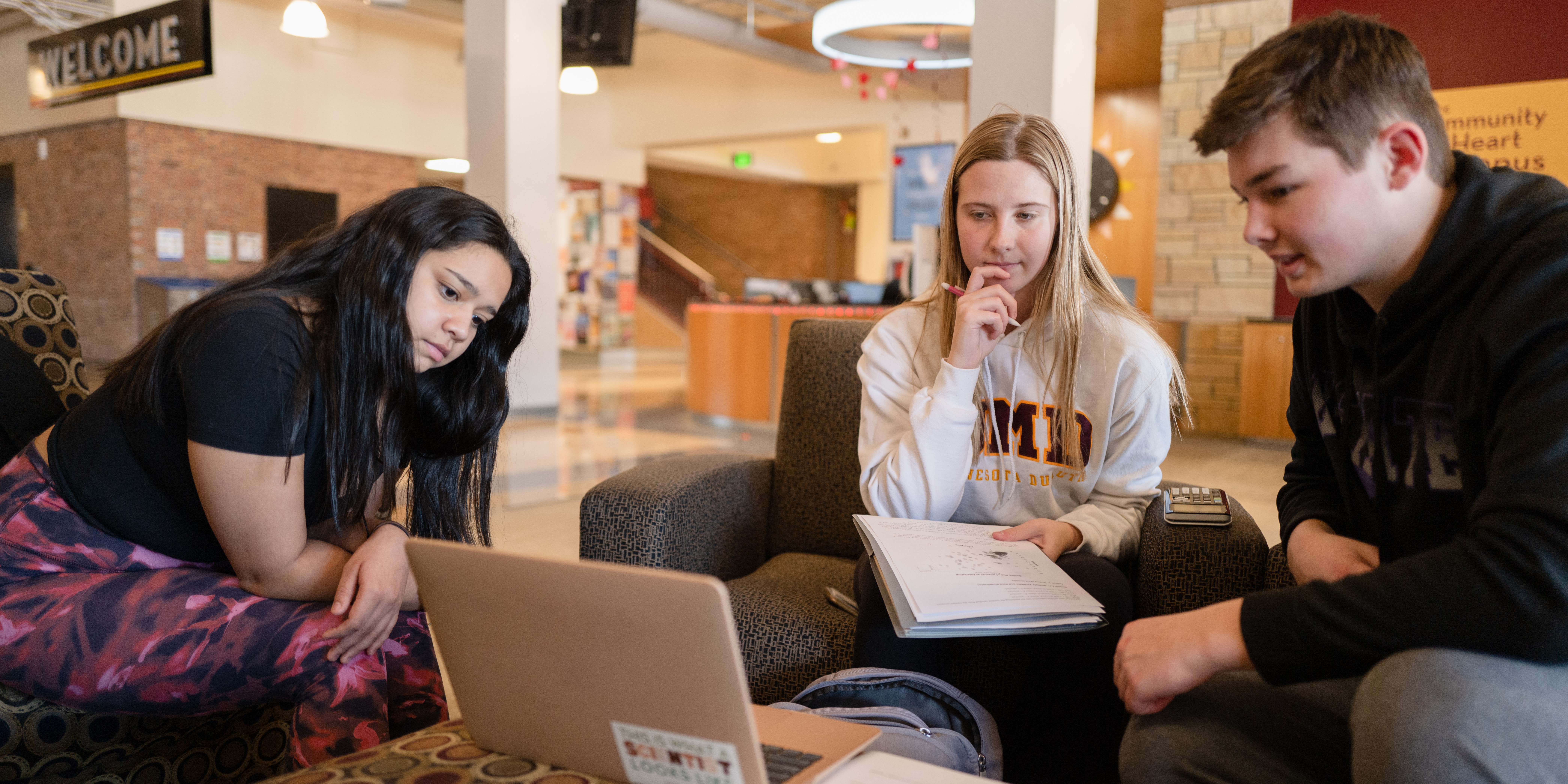 Three students sit around a laptop with notebooks in the Kirby Student Center