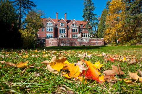 A brick mansion, with autumn leaves on the ground in foreground.